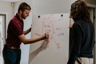 man drawing on dry-erase board by Kaleidico courtesy of Unsplash.